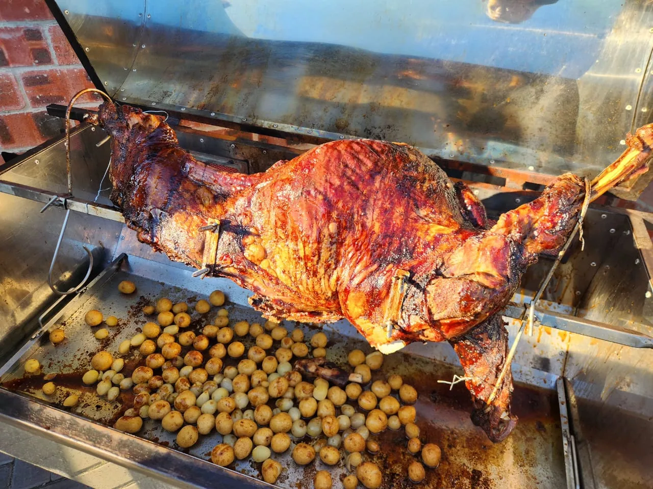 A spit braai of lamb roasting over baby potatoes.