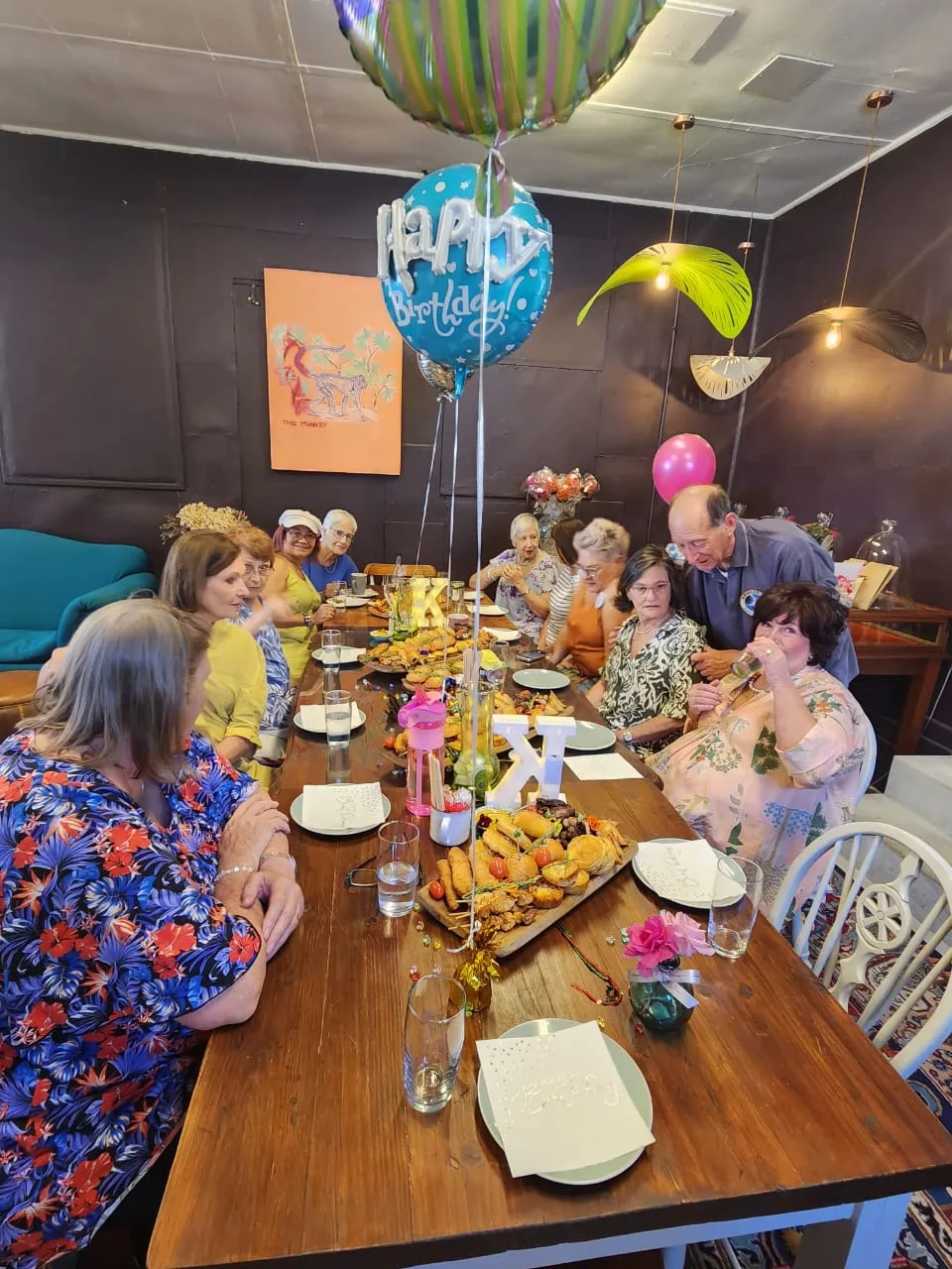 Guests gathered around a birthday table with balloons and grazing boards.